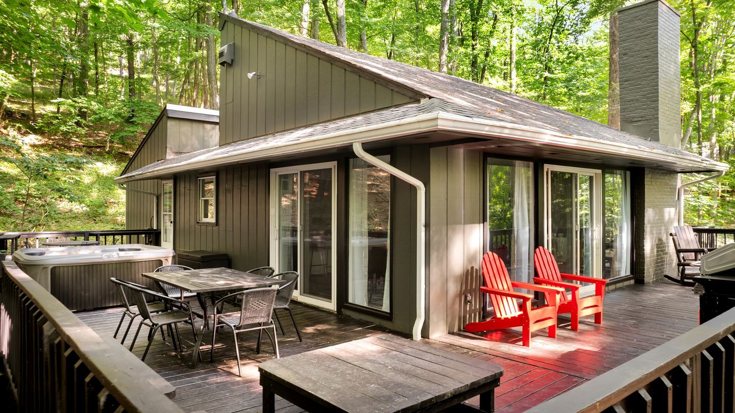 A wooden deck with outdoor furniture, a hot tub, and a covered area with red chairs.