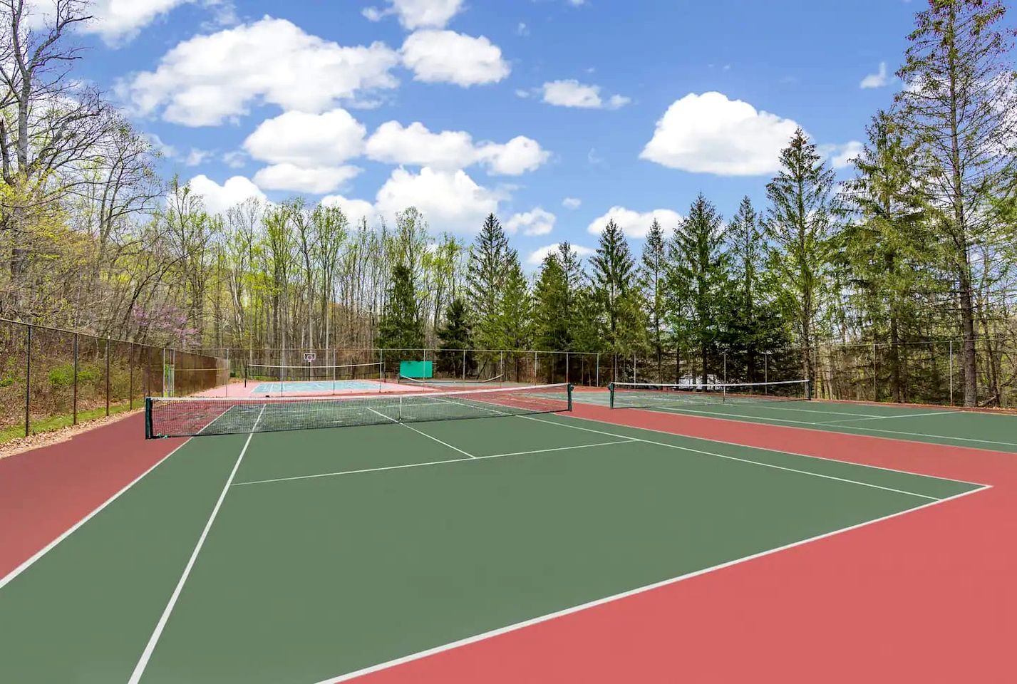 A tennis court with multiple courts, surrounded by trees and a clear sky.