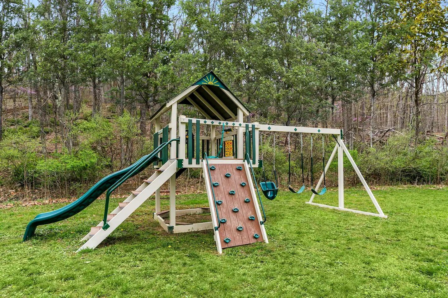 Une cabane en bois avec un toboggan et des balançoires, installée dans un espace herbeux.