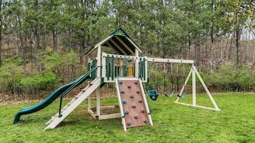 Une cabane en bois avec un toboggan et des balançoires, installée dans un espace herbeux.
