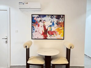 Ein Zimmer mit einer weißen Klimaanlage, einem farbenfrohen abstrakten Gemälde und zwei Stühlen mit gepolsterten Sitzflächen.