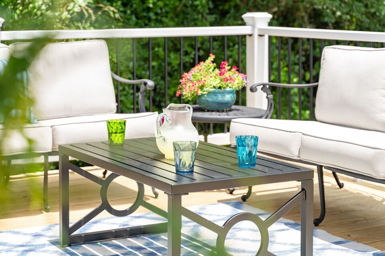 A patio with a table, two chairs, a pitcher, and a vase of flowers.