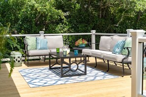 An outdoor patio with a wooden deck, two sofas with cushions, a coffee table, and a potted plant. - Salt & Serenity | Sleeps 14·Game Room·Walk to Beach (Pine Knoll Shores)