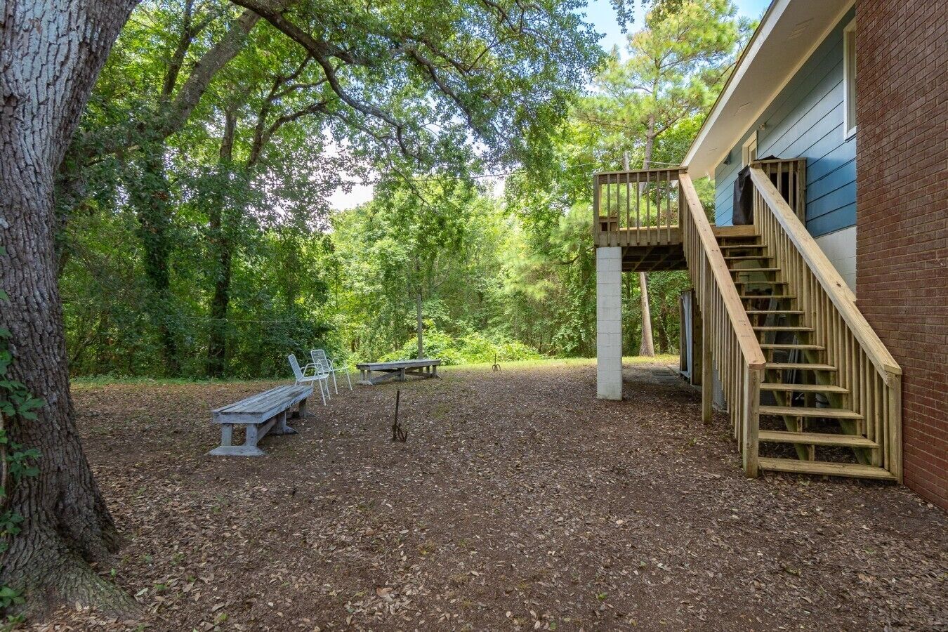 Ein überdachter Außenbereich mit einer Holztreppe, die zu einer Terrasse führt, umgeben von Bäumen und einem Kiesplatz.