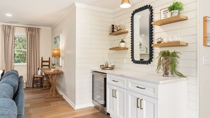 Een moderne keuken met witte kasten, een spiegel met zwarte lijst en houten planken met decoratieve objecten.