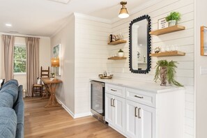 A modern kitchen with white cabinetry, a black-framed mirror, and wooden shelves with decorative items. - Salt & Serenity | Sleeps 14·Game Room·Walk to Beach (Pine Knoll Shores)
