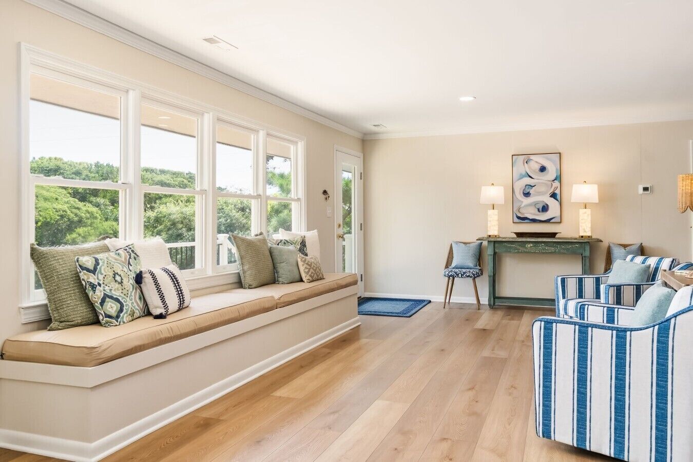 A room with a built-in bench along a large window, a blue-striped sofa, and a console table with lamps.