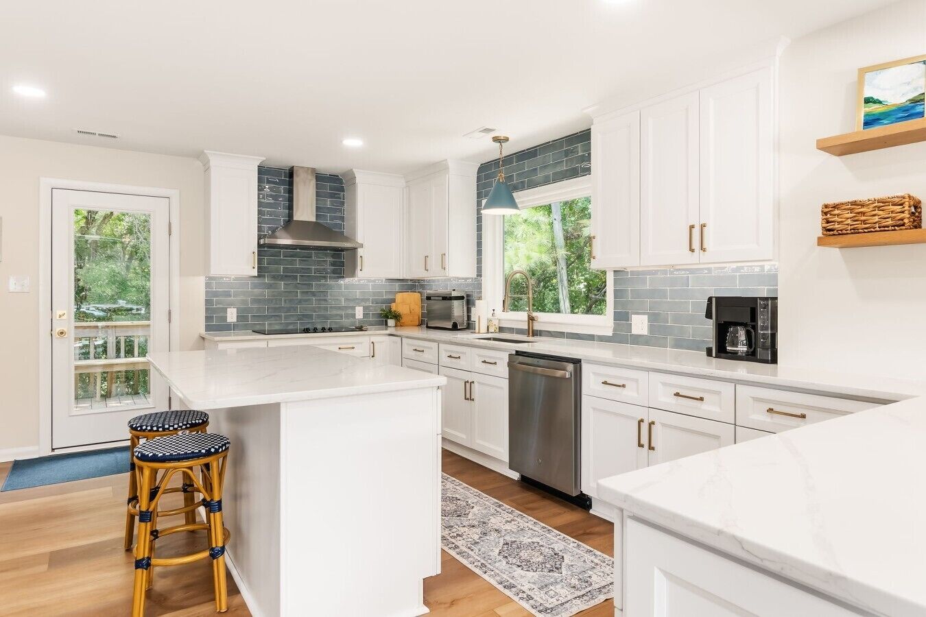 A modern kitchen with white cabinets, a large island, and a view of greenery outside.