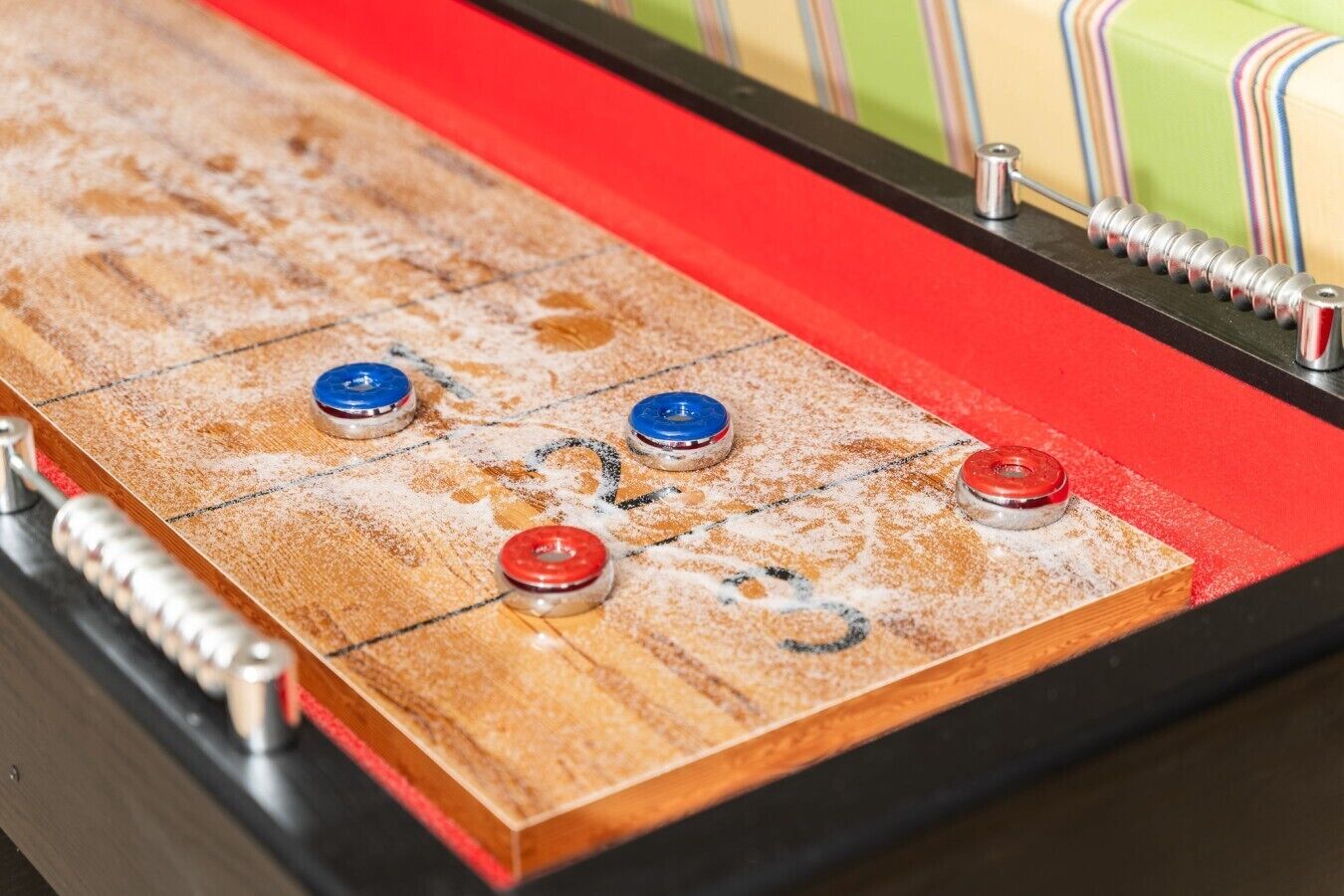 A shuffleboard table with three pucks, one blue and two red, on a wooden surface with a red border.