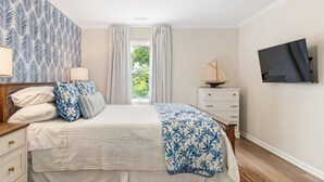 Een slaapkamer met een bed, een dressoir, een televisie en een raam met gordijnen.