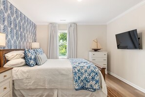 A bedroom with a bed, a dresser, a TV, and a window with curtains. - Salt & Serenity | Sleeps 14·Game Room·Walk to Beach (Pine Knoll Shores)