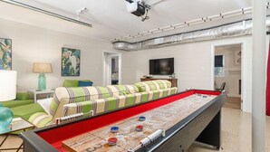 Een kamer met een tafelvoetbalspel, een bank, een televisie en een projector aan het plafond.