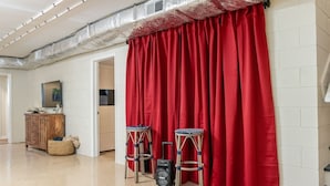 Een kamer met een rood gordijn, een houten kast en twee krukken.