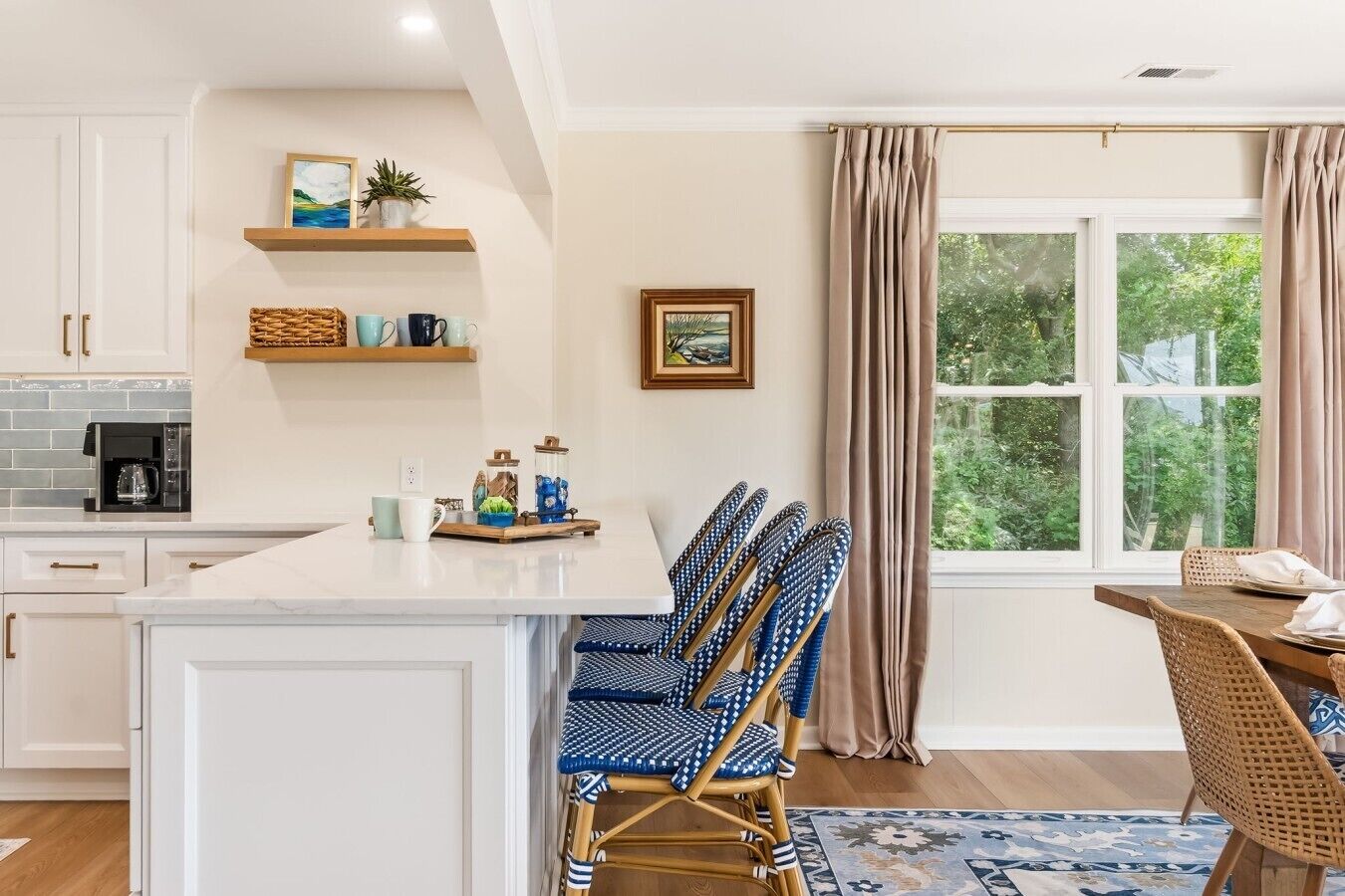 A modern kitchen with white cabinetry, a central island, and a dining area with wicker chairs.
