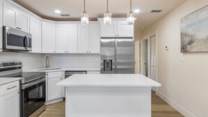 A modern kitchen with white cabinetry, stainless steel appliances, and pendant lighting.