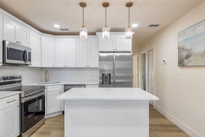 A modern kitchen with white cabinetry, stainless steel appliances, and pendant lighting.