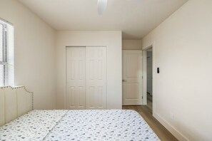 A bedroom with a bed, a door, and a window with blinds.