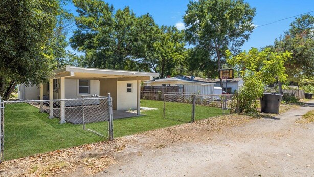 A fenced property with a small building, a basketball hoop, and a clear sky.