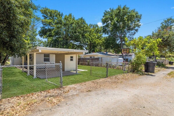 A fenced property with a small building, a basketball hoop, and a clear sky.