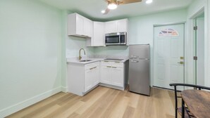 A compact kitchen with white cabinets, a stainless steel refrigerator, a microwave, and a ceiling fan.