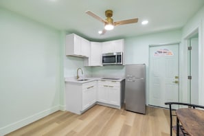 A compact kitchen with white cabinets, a stainless steel refrigerator, a microwave, and a ceiling fan.