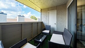 Un balcón con mobiliario de mimbre, una puerta de cristal y vista al cielo.