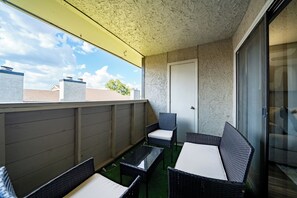 Een balkon met rieten meubilair, een glazen deur en uitzicht op de lucht.