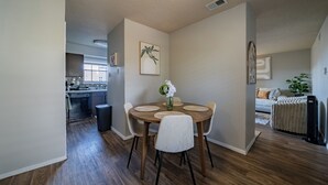 Una cocina moderna con ventana, un comedor con una mesa redonda y sillas, y una sala de estar con sofá y radiador.