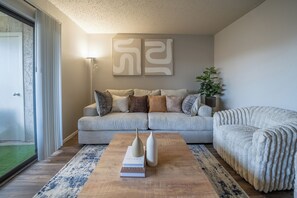Een woonkamer met een bank, een salontafel met boeken, een lamp en een plant.