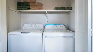 Un cuarto de lavandería con dos lavadoras de carga frontal blancas y un estante superior con toallas dobladas.