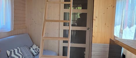 Un interior de madera con una litera, una escalera, una puerta y un pequeño escritorio.