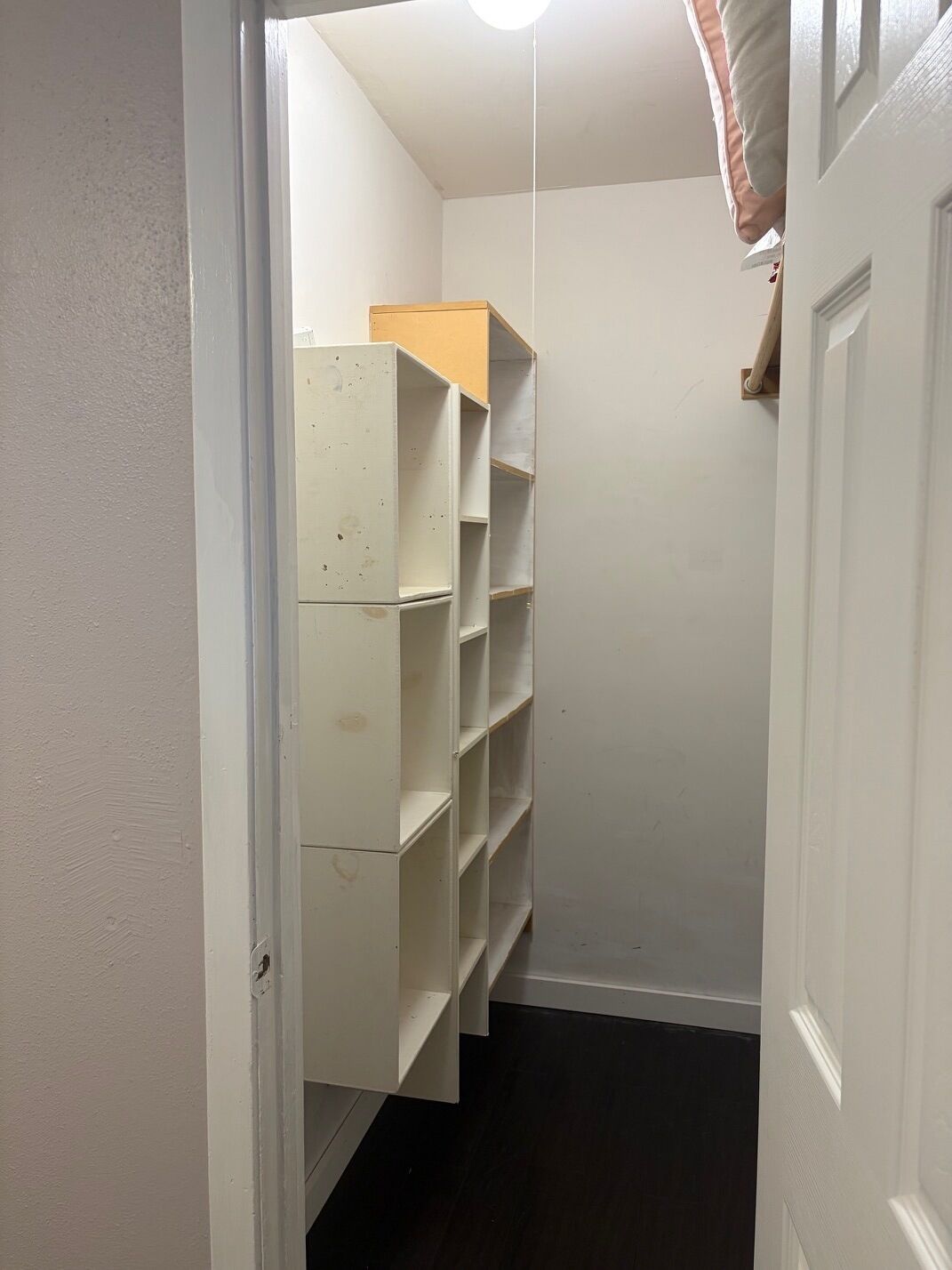 A narrow hallway with a white door on the right and a white shelving unit on the left.