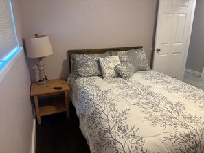 A bedroom with a bed, a nightstand, a lamp, and a door.