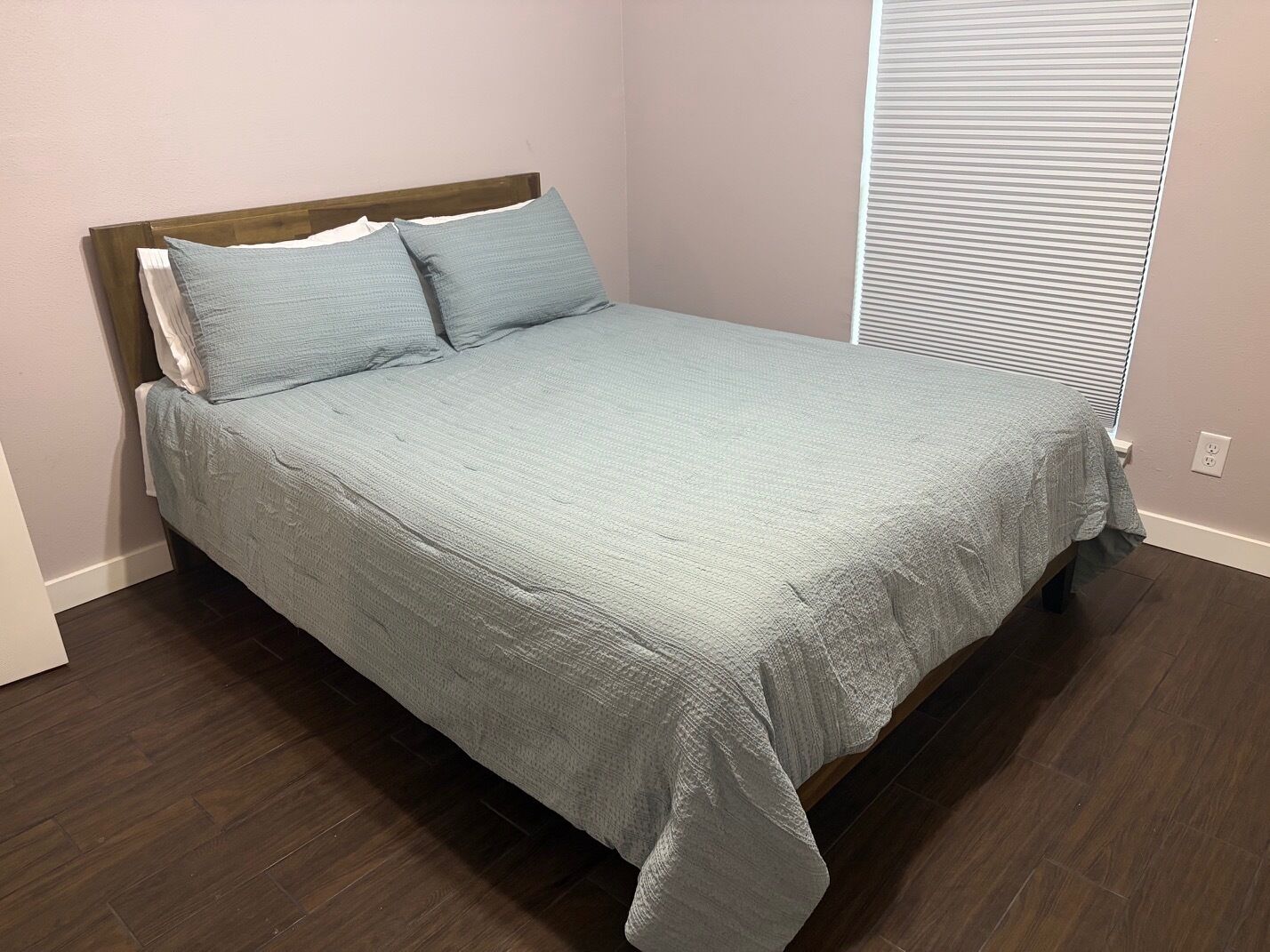 Un lit bien fait, avec une tête de lit en bois, une couvre-lit de couleur claire et deux oreillers.