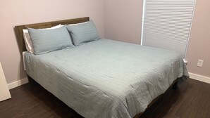 A neatly made bed with a wooden headboard, a light-colored bedspread, and two pillows.