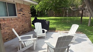 A patio with four Adirondack chairs, a barbecue grill, and a swing set.