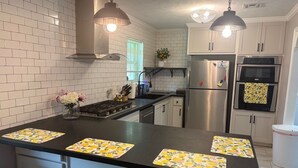 A kitchen with white tiled walls, stainless steel appliances, and a central island with bar stools.