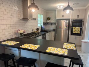 A kitchen with white tiled walls, stainless steel appliances, and a central island with bar stools.