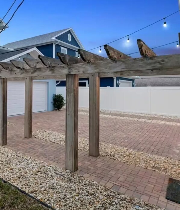 Eine Pergola aus Holz, gestützt von Holzsäulen, mit einem Kiesweg und einem blauen Gebäude im Hintergrund.