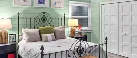 A bedroom with a bed, a ceiling fan, a window with blinds, and a door.
