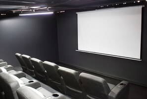 A movie theater with rows of seats, a projection screen, and a dark wall.