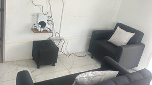 A living room with a flat-screen TV mounted on the wall, two black armchairs, a small ottoman, and a white tiled floor. - Spacious 5-bedroom MANSION in tranquil Guarne perfect for families & events (Guarne)