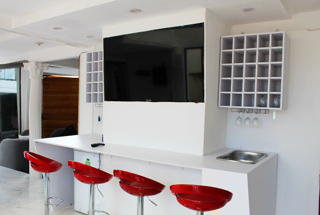 Une cuisine moderne dotée d’un téléviseur encastré, d’un coin bar avec des tabourets rouges et d’un meuble à vin.