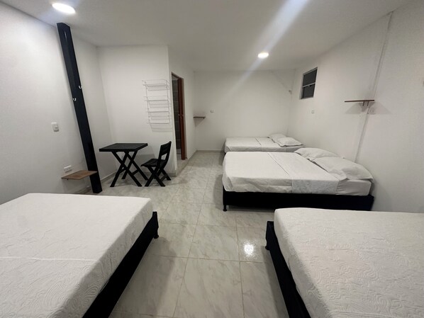 A room with three beds, a small table, and a chair.