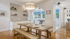 A dining area with a wooden table set for four, a bench, and a pendant light. - The Grand Carolina | Golf Cart ·Hot Tub ·4BR ·PKS (Pine Knoll Shores)