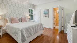 A bedroom with a bed, nightstands, a ceiling fan, a window, a door, and a television. - The Grand Carolina | Golf Cart ·Hot Tub ·4BR ·PKS (Pine Knoll Shores)