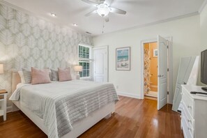 Ein Schlafzimmer mit Bett, Nachttischen, Deckenventilator, Fenster, Tür und Fernseher.