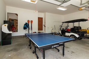 Ein Tischtennis-Tisch in einem Raum, der einen Golfwagen, einen weiteren Tischtennis-Tisch und eine Tür zeigt.