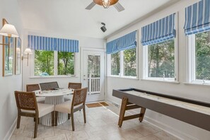 Ein Zimmer mit Pooltisch, Esstisch, Stühlen und großen Fenstern mit blauen, gestreiften Vorhängen.
