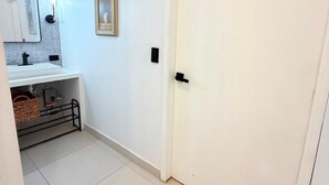 A bathroom with a white sink, a mirror, a framed picture on the wall, and a white door.